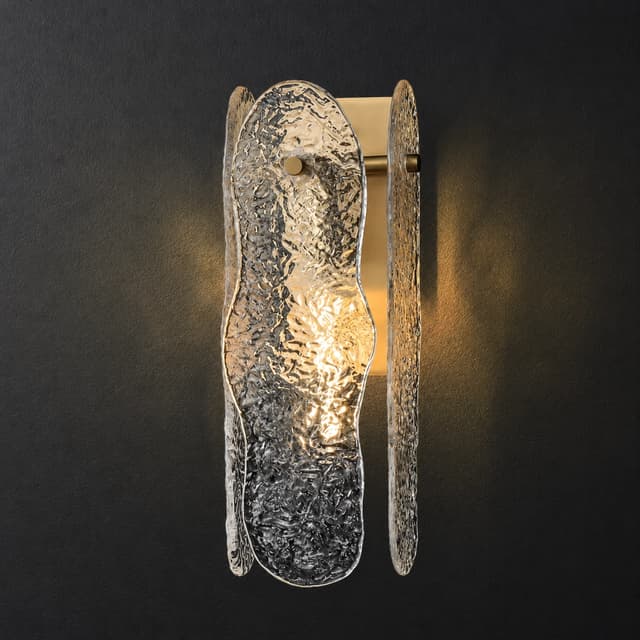 Sculptural brass textured glass wall sconce illuminated against a dark wall