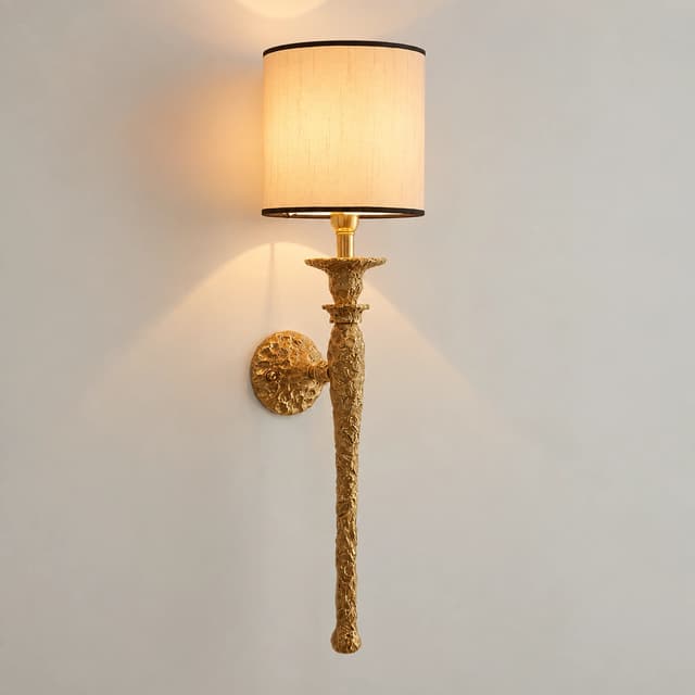 Illuminated antique gold copper wall sconce with an ivory fabric drum shade and ornate elongated metal body