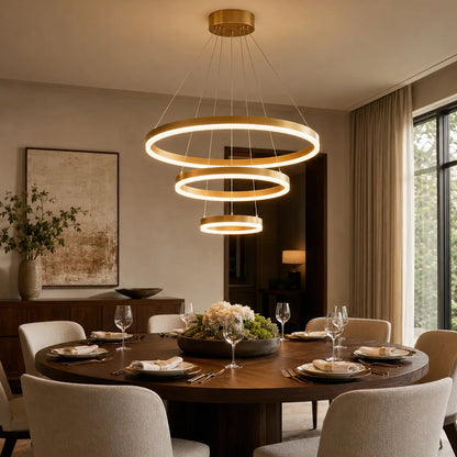 Modern gold LED ring chandelier glowing above a round dining table in a warm apartment dining room