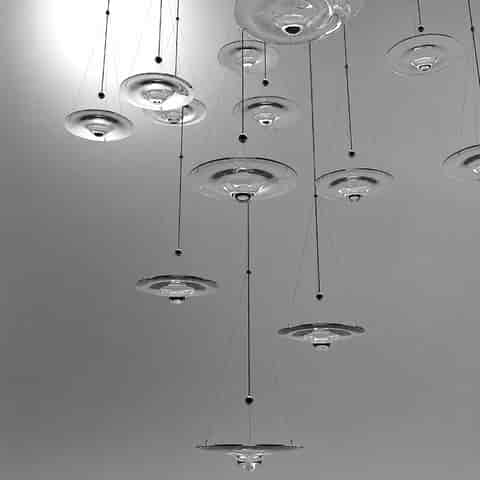 Cluster of clear glass disc pendant lights with floating saucer shaped shades, slim suspension cables and minimalist metal details