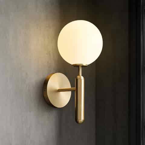 Angled view of a brass finish globe wall sconce with round backplate and opal glass shade