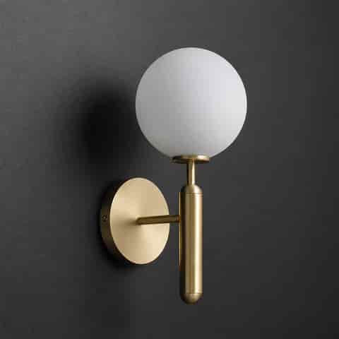 Modern brass globe wall sconce with soft ambient glow on a textured gray wall
