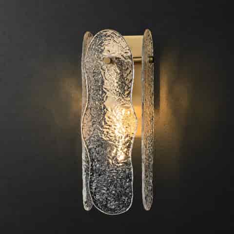 Sculptural brass textured glass wall sconce illuminated against a dark wall