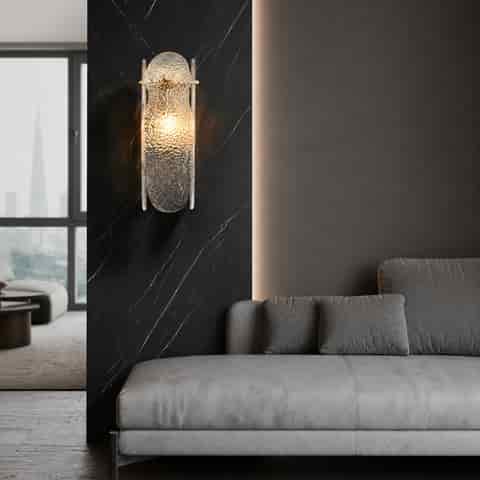 Modern brass and textured glass wall sconce installed on a dark marble accent wall