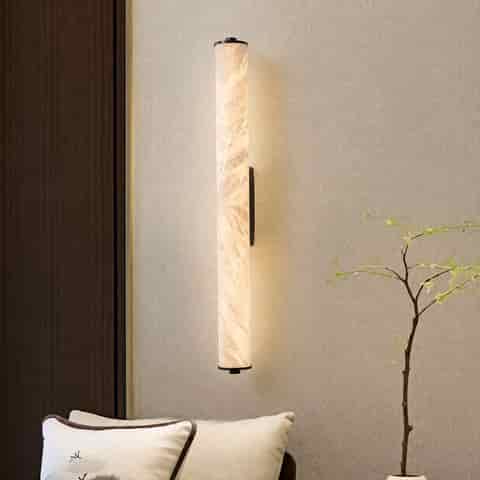 Vertical translucent stone look wall sconce beside a lounge chair and indoor plant