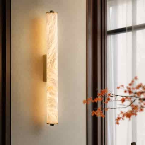 Brass vertical cylinder wall sconce with warm diffused light beside a window