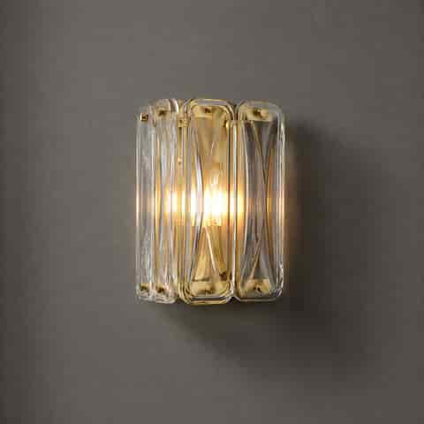 Compact brass and clear glass block wall sconce with warm ambient light