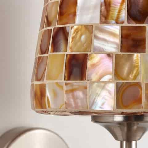 Illuminated mother of pearl mosaic wall sconce casting a warm ambient glow in a modern interior