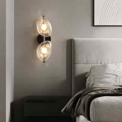 Clear textured glass double wall sconce beside a modern bedroom bed with warm ambient lighting