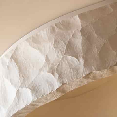 Close up of a textured ivory resin and acrylic flush mount ceiling light with a soft warm ambient glow