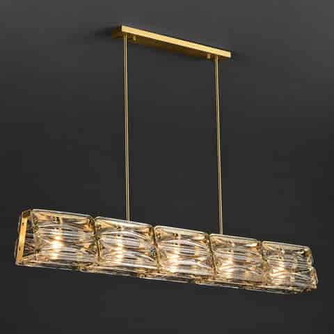 Gold copper and clear textured glass linear chandelier glowing warmly against a dark background