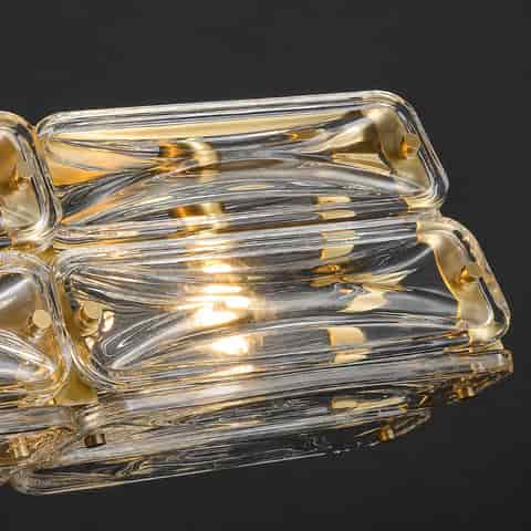 Close up of thick clear textured glass blocks on a gold copper linear chandelier with sculpted ripple details