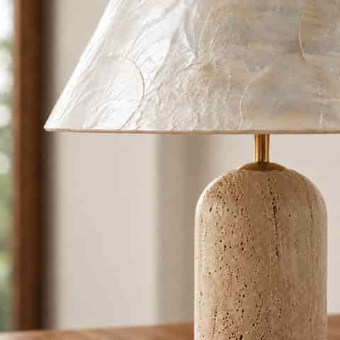Close up of a natural seashell table lamp shade with pearlescent ivory shells and a textured warm beige base
