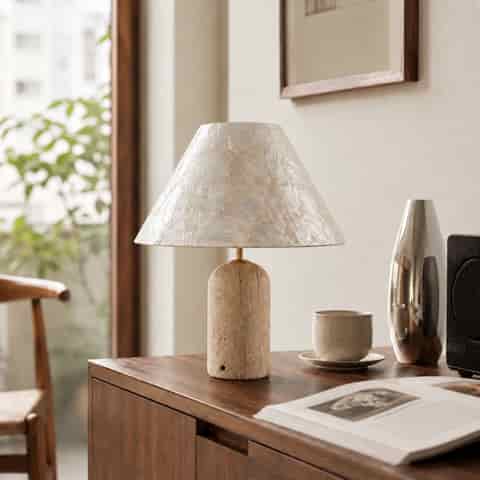 Seashell table lamp glowing warmly on a wood console with an ivory shell shade and textured beige base