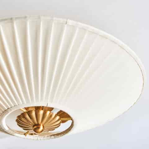 Close up of the ivory pleated fabric shade with radial folds and copper tone floral metal detail