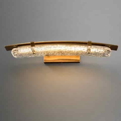 Linear brass wall sconce with curved textured glass diffuser in horizontal installation