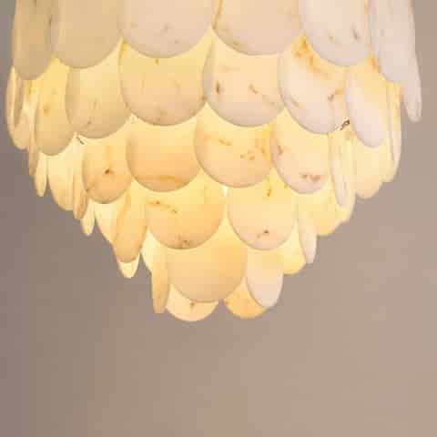Close up of illuminated faux alabaster chandelier with overlapping white marble look discs and warm diffused glow