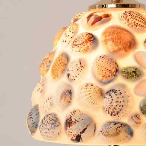 Close up of a translucent shell and glass table lamp shade featuring natural shell patterns in ivory, amber, brown, and green tones
