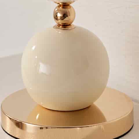 Close up of the glossy ivory ceramic sphere and polished gold metal base of a decorative seashell table lamp