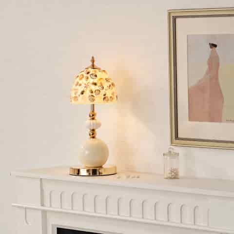 Coastal glam seashell table lamp glowing warmly on a white console with an ivory ceramic base and polished gold details