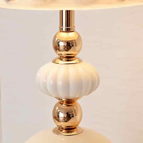 Close up of the ivory ceramic fluted ornament and polished gold spherical accents on a decorative shell table lamp