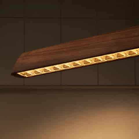 Close up of walnut wood grain linear pendant with clear prismatic LED lens array along the underside