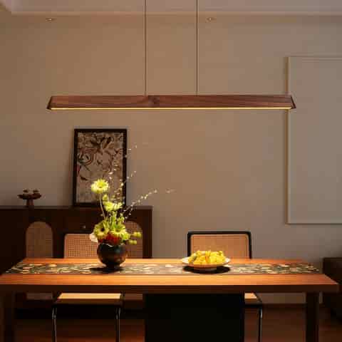 Long walnut finish linear pendant light centered above a rectangular dining table in a warm modern dining room
