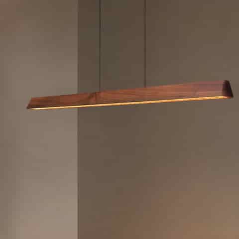 Close view of a slim walnut finish linear LED pendant with suspended dual cable installation and warm downward light