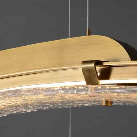 Close up of copper chandelier frame, curved mounting bracket and textured clear glass diffuser with warm glow