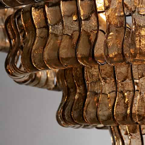 Close up of amber toned textured glass chandelier panels with curved edges and warm light reflections