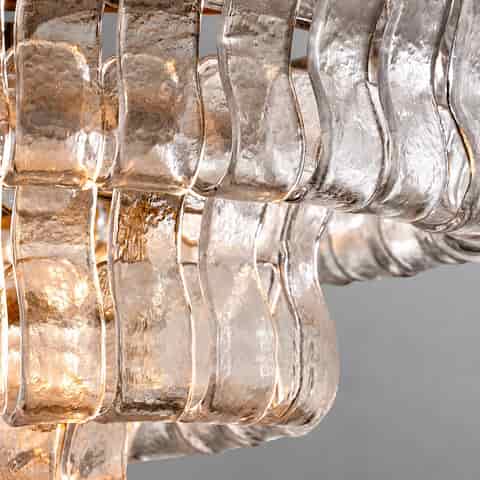 A close up of a textured, clear glass pendant light panel with curved edges, reflecting a warm glow