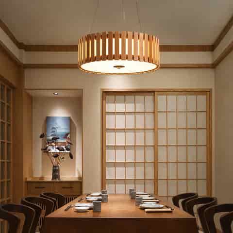Modern wooden drum chandelier with vertical slats suspended above a dining table