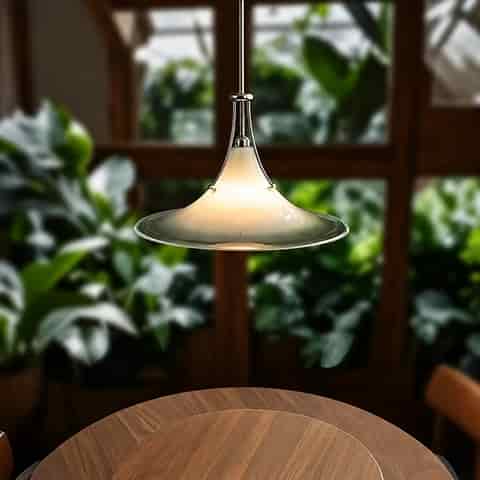 Frosted glass saucer pendant light with a clear rim, polished metal frame and warm glow above a round dining table