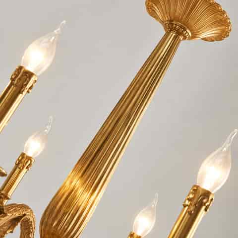 Detailed view of a gold chandelier with fluted central column, floral ornamentation and illuminated candle style bulb