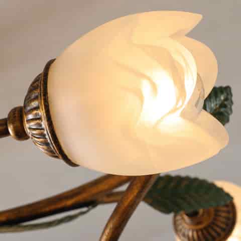 Close up of a frosted white flower shaped light shade with a warm glowing bulb and decorative metal socket