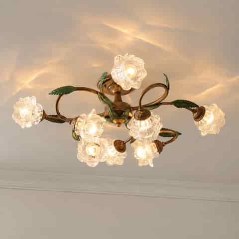 Underside view of a vintage botanical ceiling light with curved metal arms, green leaves, and glowing flower shaped shades