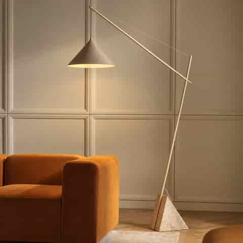 Contemporary sculptural cantilever floor lamp with an ivory beige iron frame, triangular marble base and tapered iron shade beside a sofa