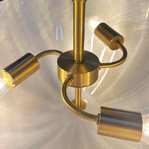 Close up of the natural copper fixture with curved arms, cylindrical bulb holders and a sculptural fluted glass diffuser
