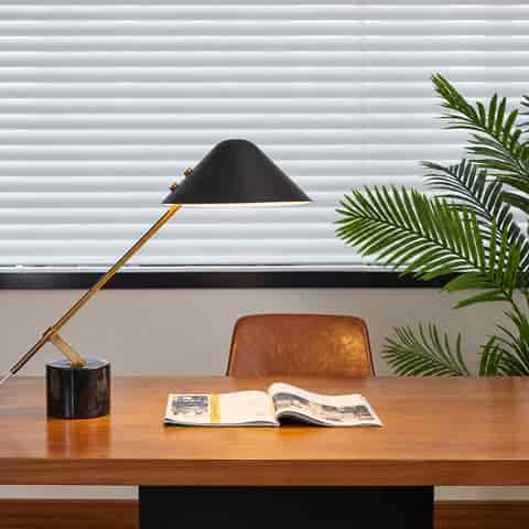 Black cantilever table lamp with a dark stone base, polished gold arm and wide conical metal shade