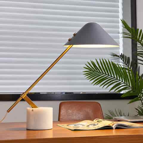 Gray cantilever table lamp with an ivory stone base and polished gold metal arm in a modern workspace