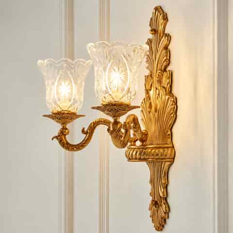 Elegant antique gold two light wall sconce with ornate curved arms and decorative clear glass shades