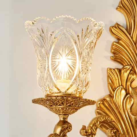 Close up of decorative clear glass wall sconce shade with floral cut pattern and warm illumination
