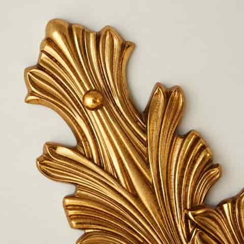 Close up of ornate gold leaf shaped wall sconce backplate with raised decorative detailing