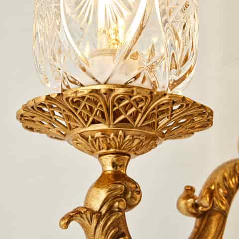 Vintage gold two light wall sconce with ornate leaf motifs and illuminated clear glass shades